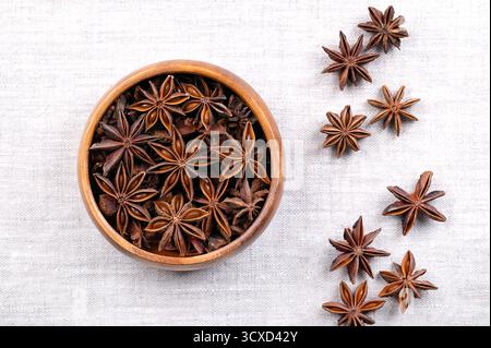 Aggiungere i semi di anice in una ciotola di legno su lino. Frutti di Illicium verum, noto anche come badiano, anice stellato cinese, anice stellato. Foto Stock