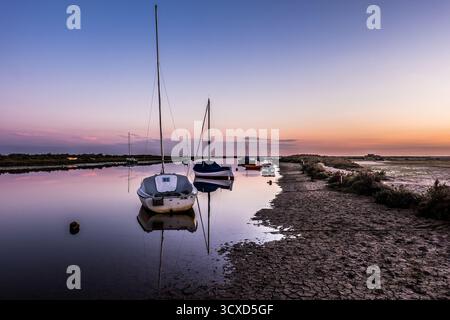 Barche ormeggiate con la bassa marea sul canale Blakeney a Norfolk all'alba con riflessi in acque calme Foto Stock