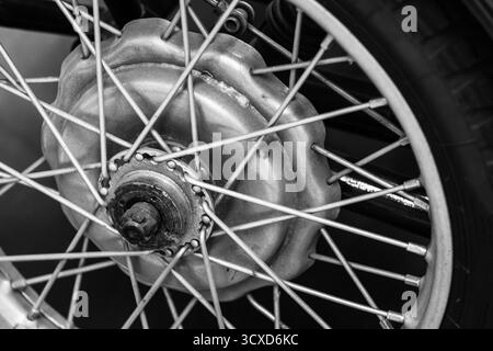 Una vista dettagliata in bianco e nero del mozzo della ruota della motocicletta, delle razze, del cerchione e dell'assale. L'immagine monocromatica enfatizza la texture del metallo e. Foto Stock