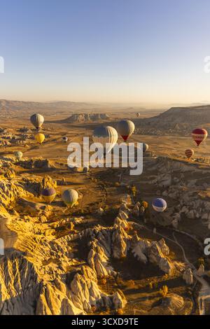 Cappadocia, Turkiye - 06 novembre 2022: Vista delle mongolfiere che si spostano sul paesaggio surreale, gettando lunghe ombre attraverso le valli e i caratteristici camini delle fate. Foto Stock
