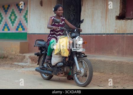 Una donna tribale rurale vista su uno scooter durante una festa della comunità nel villaggio. Le donne rurali tribali del villaggio di Ghatsila partecipano a una danza tradizionale durante un evento culturale locale che mostra le usanze della comunità e l'arte popolare. La giornata internazionale delle donne rurali si celebra ogni anno il 15 ottobre e mette in evidenza il ruolo vitale delle donne rurali nella produzione alimentare, nell'agricoltura e nella gestione ambientale. A livello globale, le donne costituiscono oltre il 35 per cento della forza lavoro agricola, raggiungendo oltre il 50 per cento in alcune parti dell'Africa e dell'Asia, eppure spesso si trovano ad affrontare un accesso iniquo alla terra, al credito e alla tecnologia. Il giorno Foto Stock