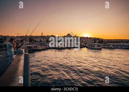 Istanbul, Turkiye - 2 ottobre 2019: Vista del Ponte di Galata pieno di attività, mentre il sole tramonta getta un bagliore dorato sulla moschea Yeni Cami. Foto Stock