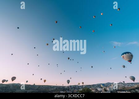 Goreme, Turkiye - 09 ottobre 2019: Vista di una moltitudine di mongolfiere che fluttuano pacificamente sopra il paesaggio unico della Cappadocia, punteggiando il cielo color pastello dell'alba con vivaci sfumature. Foto Stock