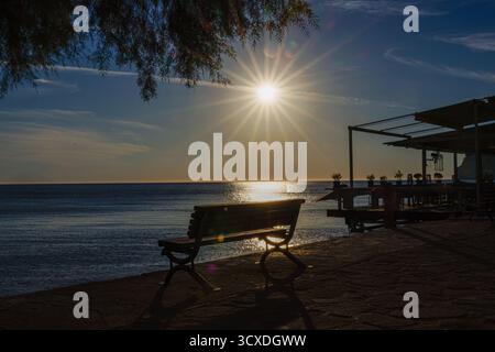 Una tranquilla vista sul mare al tramonto con una panchina e un molo. Foto Stock