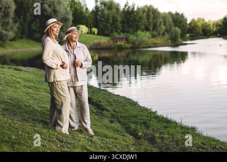 Due donne anziane che viaggiano in riva al lago in un paesaggio panoramico, godendo di luce soffusa e vista sulla natura, tranquille all'aperto. Foto Stock