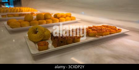 Pasticceria assortita e ciambelle esposte su vassoi bianchi in una panetteria. Foto Stock