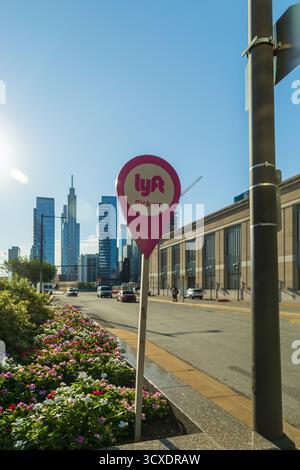 Un cartello rosa LYFT è su un palo di fronte a un edificio. Il cartello si trova su una strada con auto e poche persone, Philadelphia, USA Foto Stock
