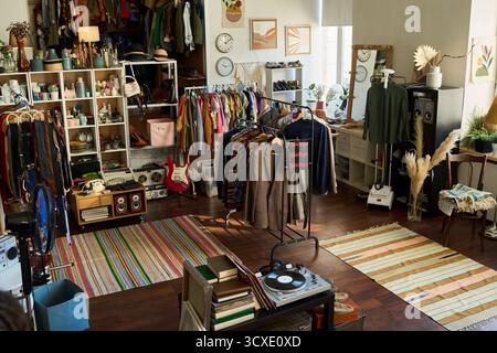 Abbigliamento e accessori vintage esposti su scaffali e scaffali all'interno del negozio, vari indumenti e articoli retrò messi in vendita, luce solare che scorre attraverso le finestre, nessuna persona visibile Foto Stock