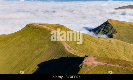 Escursionisti che camminano sulla cima della montagna Pen-y-fan sopra uno strato di nebbia e nuvole Foto Stock