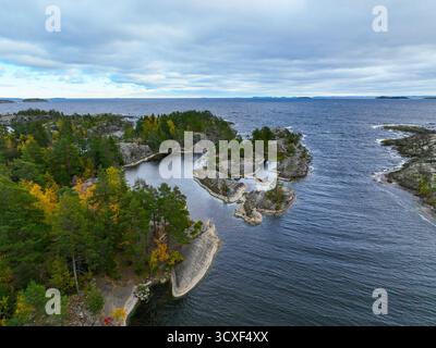 Vista rialzata di una piccola insenatura con rocce lisce e un gruppo di isole ricoperte di alberi, che si collegano a un'ampia distesa di acque blu scuro e ruvide Foto Stock