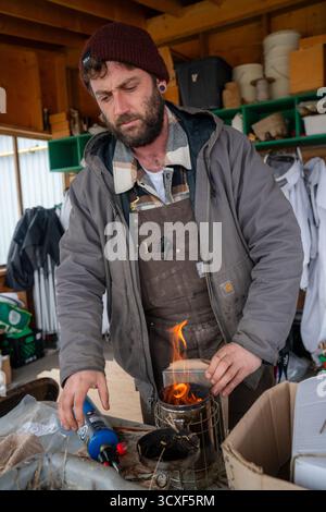 Un apicoltore prepara un fumatore utilizzando una torcia all'interno di uno spazio di lavoro in legno presso la Dancing Bee Farm prima di ispezionare gli alveari durante la manutenzione primaverile Foto Stock
