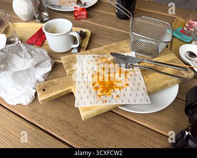 Svuotate i vari piatti sporchi e i tovaglioli usati su un tavolo di legno in un bar dopo un pasto Foto Stock