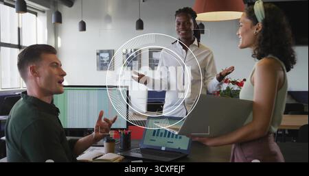 Tre colleghi in abbigliamento formale discutono informazioni alla scrivania in ufficio, con monitor per notebook Foto Stock