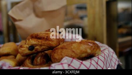 Esporre il cestino di vimini riempito con dolci all'uvetta sul bancone della panetteria con un panno rosso e bianco Foto Stock