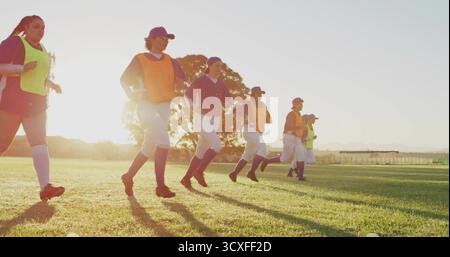 Sette giocatori di softball che si riscaldano sul campo da softball sotto il sole, indossando pinnie e scarpe da calcio Foto Stock