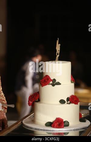 Un'incredibile torta nuziale bianca a tre piani decorata con rose rosse fresche, che simboleggia eleganza, amore e celebrazioni senza tempo. Foto Stock
