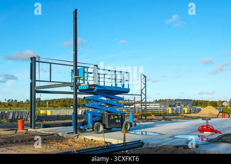 Un sollevatore a forbice in un cantiere con telai in acciaio e materiali da costruzione. Apparecchiature industriali per edilizia, ingegneria e sviluppo pr Foto Stock