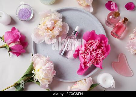 Bottiglie di olio essenziale con candele, sale marino, strumento per massaggi guasha e bellissimi fiori di peonia su sfondo chiaro Foto Stock