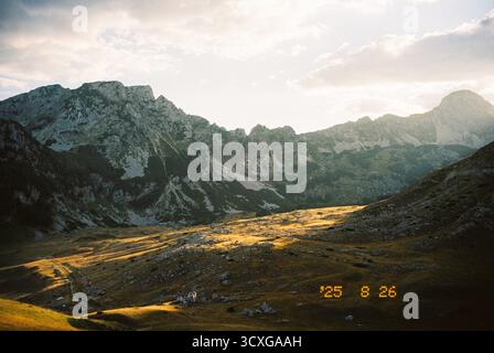 Valle di montagna illuminata dal sole con pendii rocciosi e vette spettacolari sotto un cielo parzialmente nuvoloso in un film Foto Stock