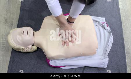 Addestramento RCP sul manichino medico. Persona che pratica le compressioni toraciche durante la sessione di addestramento per la RCP utilizzando un manichino medico su un tappetino grigio Foto Stock