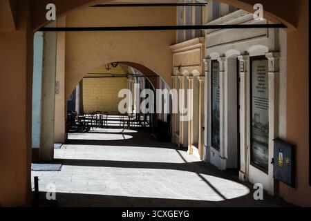 classici portici rinascimentali con accoglienti sedie da caffè e tavoli sullo sfondo che gettano ombre sul pavimento Foto Stock