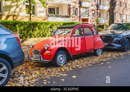 Auto Citroen 2CV rossa d'epoca parcheggiata in strada circondata da foglie autunnali gialle e marroni cadute Foto Stock