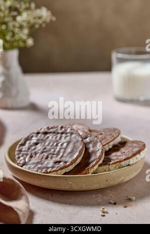 piatto di crocchette di riso torte e biscotti ricoperti di cioccolato al latte e un bicchiere di latte su sfondo beige Foto Stock