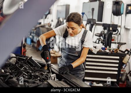 Una meccanica esperta sta lavorando su un motore di un'auto in un'officina dedicata alla riparazione dei veicoli Foto Stock
