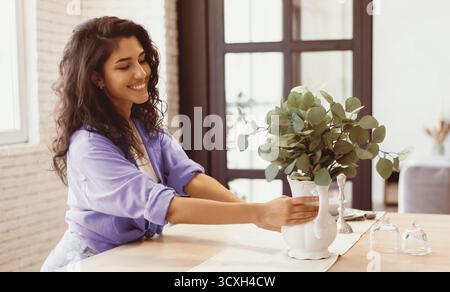Donna che organizza l'eucalipto in un vaso in un accogliente spazio interno Foto Stock
