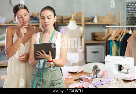 Due sarte che disegnano un modello di vestiti su un tablet Foto Stock