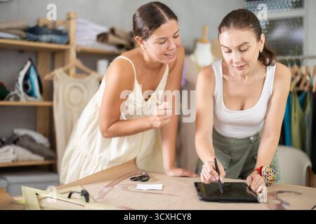 Due sarte che disegnano un modello di vestiti su un tablet Foto Stock