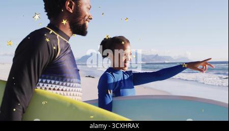 Surfisti in piedi che indossano mute che tengono tavole da surf sulla spiaggia sabbiosa, puntando verso l'orizzonte dell'oceano Foto Stock