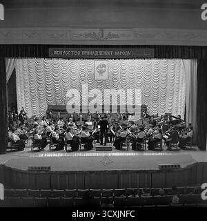 Una foto d'archivio del 1984 mostra un'orchestra sinfonica che si esibisce sul palco del Palazzo della Cultura Artem a Sloviansk, RSS Ucraina. Un direttore conduce i musicisti prima di un pubblico seduto nella sala. Sopra il palco, un'importante insegna mostra il classico slogan leninista, "l'arte appartiene al popolo". La scena cattura la ricca vita culturale di una tipica città industriale sovietica. Questa immagine è un prezioso documento di arti ed eventi della comunità in un pacifico Donbas prima della guerra Foto Stock