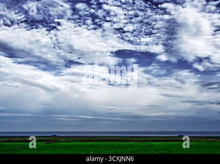 Nuvole cupe che convergono su ampie paludi verdi raggiungendo il tranquillo confine settentrionale del mare sotto un paesaggio che cambia il cielo Foto Stock