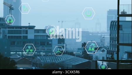 Icone esagonali galleggianti che mostrano idee di energia verde sopra le ringhiere nello skyline urbano con gru Foto Stock