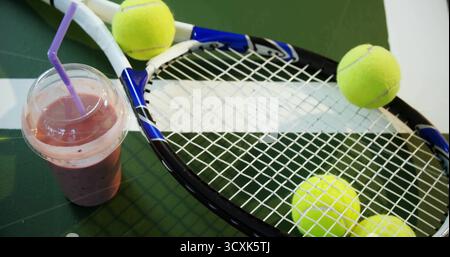 Racchetta da tennis blu sul tavolo da ping pong con palle da tennis gialle e coppa per frullati di paglia viola Foto Stock