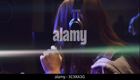 Artista che canta indossando le cuffie e tenendo il microfono condensatore in cabina, striature leggere Foto Stock