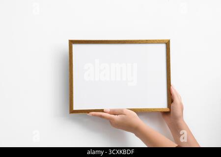 Donna che appende una cornice vuota per diplomi su un muro bianco, primo piano. Mockup per il design Foto Stock