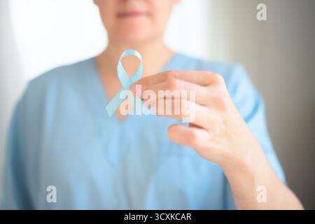Infermiera donna in uniforme medica che tiene il nastro blu a portata di mano. Simbolo della consapevolezza del cancro alla prostata, mese di novembre di prevenzione, diagnosi precoce, assistenza sanitaria e supporto per i pazienti. Foto Stock