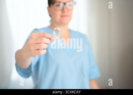Primo piano di lavoratore medico donna in uniforme con nastro blu a portata di mano. Consapevolezza del cancro alla prostata, prevenzione a novembre, supporto sanitario e rilevamento di malattie oncologiche. Foto Stock