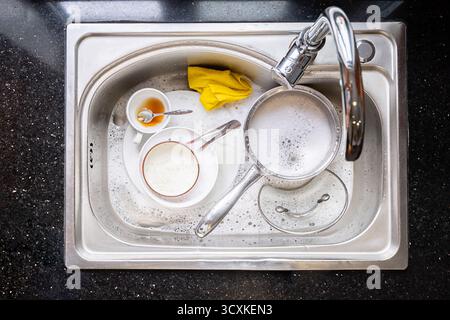 Piatti sporchi nel lavandino della cucina riempiti di acqua e sapone. Pila di stoviglie non lavate in attesa di essere pulite. Concetto di lavoro domestico quotidiano. Foto Stock
