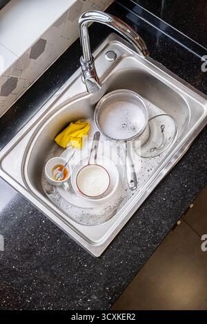 Piatti sporchi con acqua saponata nel lavandino della cucina. Concetto di lavoro domestico che prevede il lavaggio dopo pasto per le operazioni di pulizia quotidiane. Foto Stock