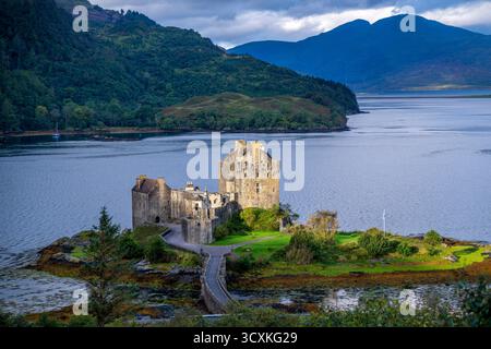 Il castello di Eilean Donan sorge su un'isola lussureggiante in un tranquillo lago, con colline ondulate e cieli spettacolari. Ideale per scene storiche, paesaggistiche o di viaggio. Foto Stock