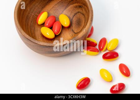 Capsule di gelatina morbida rosse e gialle in una ciotola di legno su fondo bianco Foto Stock