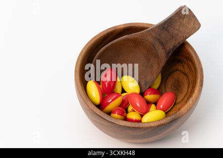Capsule di gelatina rosse e gialle morbide in una ciotola di legno con un cucchiaio di legno Foto Stock