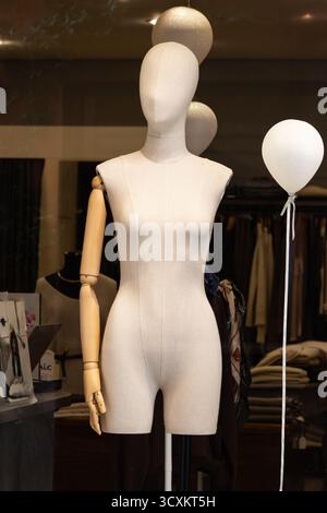 Elegante manichino sartoriale con braccio in legno si stende graziosamente in una boutique di moda circondata da abiti eleganti e riflessi di luce soffusa. Foto Stock