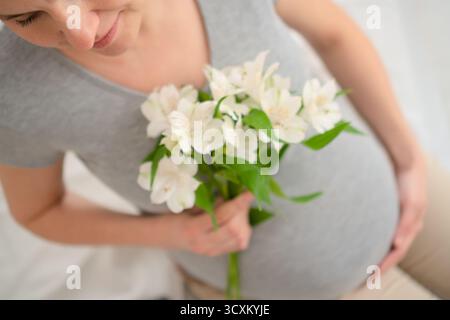 I delicati fiori bianchi completano la delicata carezza della pancia della mamma. Intimo momento di gioia della gravidanza e bellezza naturale. Foto Stock