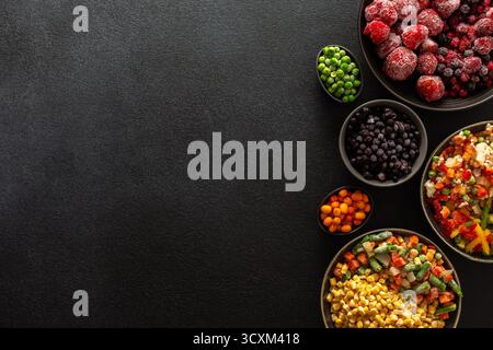 Una varietà di verdure e frutta congelate disposte in piatti, su sfondo scuro, catturando l'essenza della conservazione estiva per i pasti invernali Foto Stock