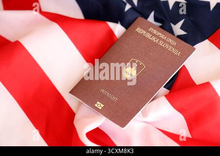 Passaporto sloveno sulla grande bandiera ondulata degli Stati Uniti d'America primo piano. Concetto di immigrazione e visto PER GLI STATI UNITI Foto Stock