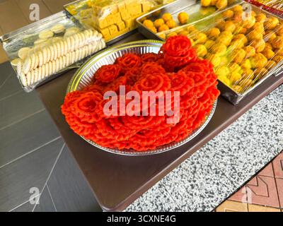 Un tavolo con vari dolci tradizionali indiani, tra cui pile di jalebi rossi accanto a vassoi di prelibatezze avvolte. Foto Stock